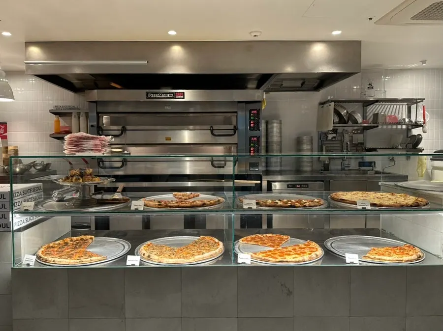 Glass display case of pizza slices and open kitchen