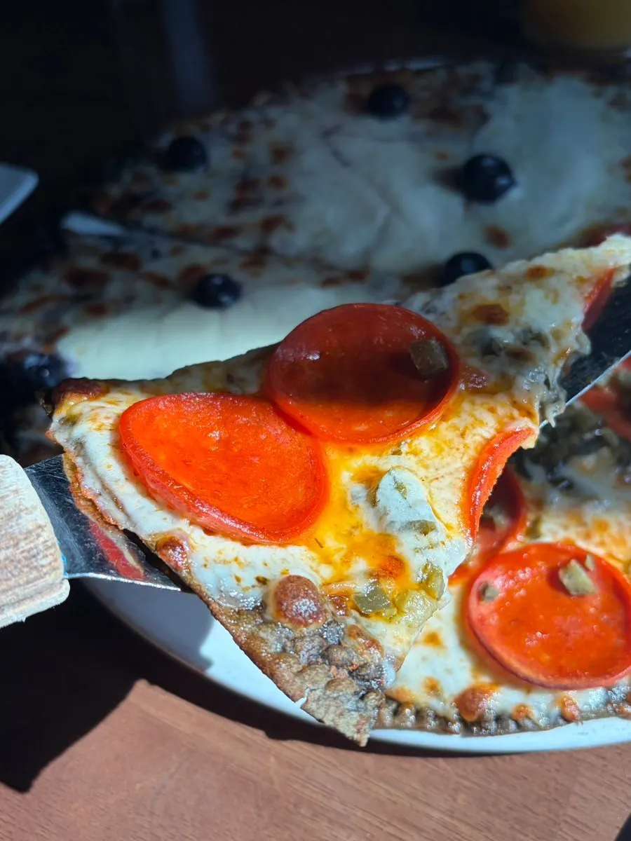 Slice of half-and-half pizza with thin crust piled with toppings