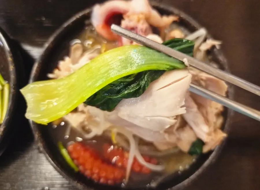 A piece of chicken topped with vegetables and kimchi