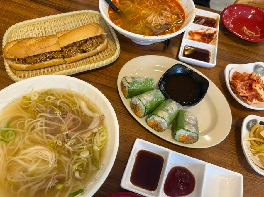 Full spread of two bowls of pho, spring rolls, and banh mi