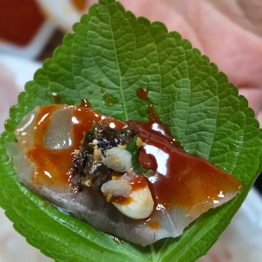 Sashimi topped with dried seaweed flakes on a perilla leaf