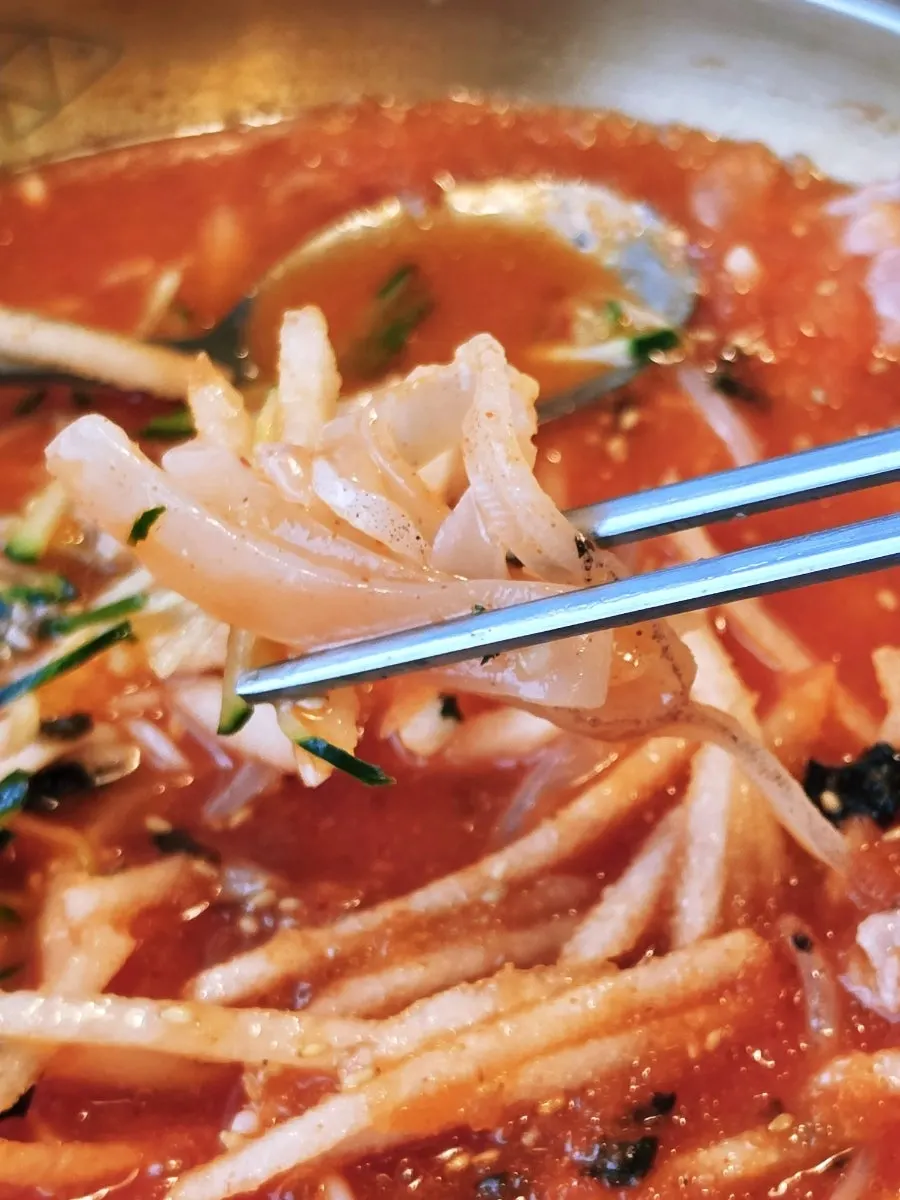 Chopsticks lifting squid sashimi with pear and cucumber