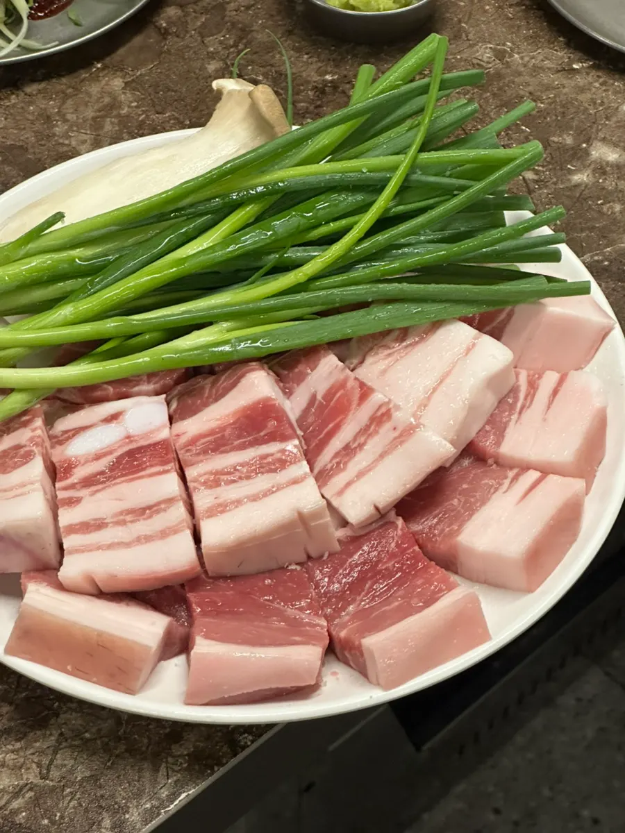 Plate of rosy-pink raw Nanchuk Matdon black pork with scallions and mushrooms