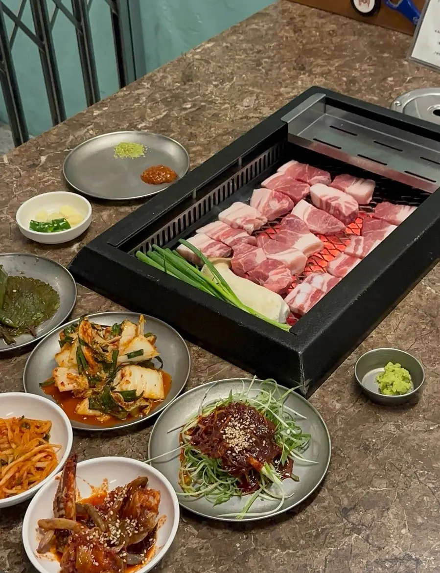 Charcoal grill with scallions and mushrooms cooking alongside the pork