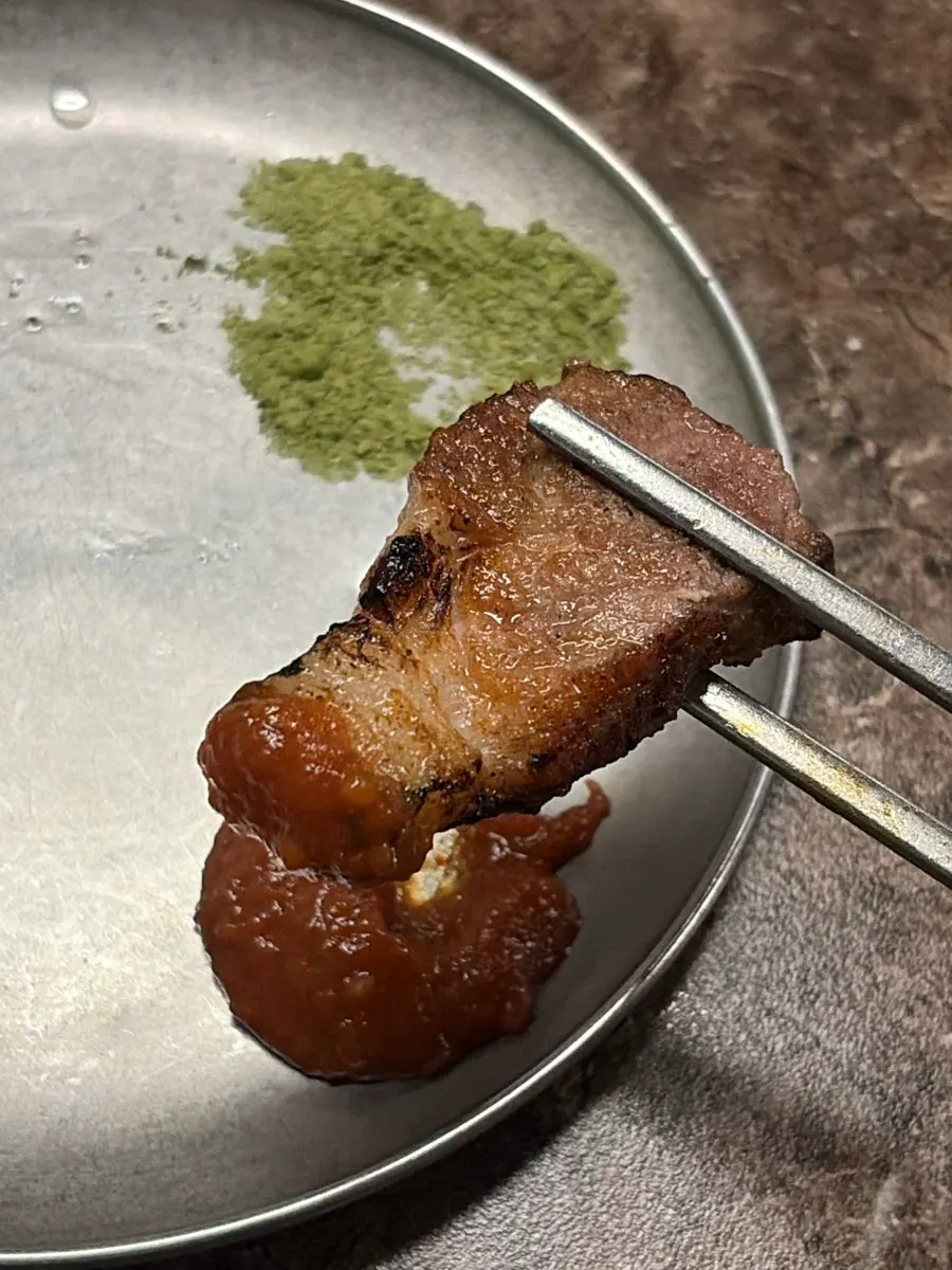 A piece of black pork dipped in matcha salt
