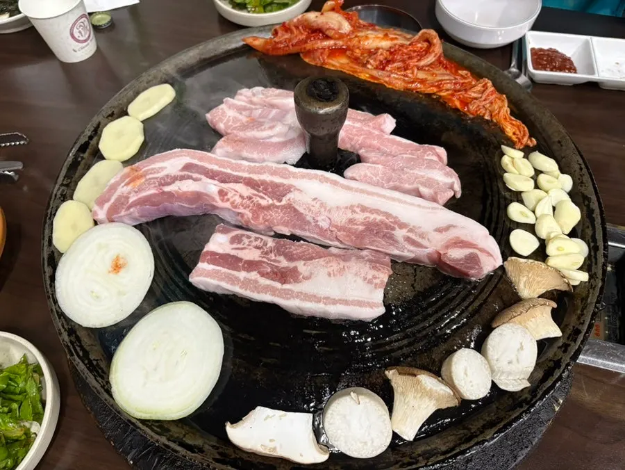 Staff member grilling pork belly on the cauldron-lid grill