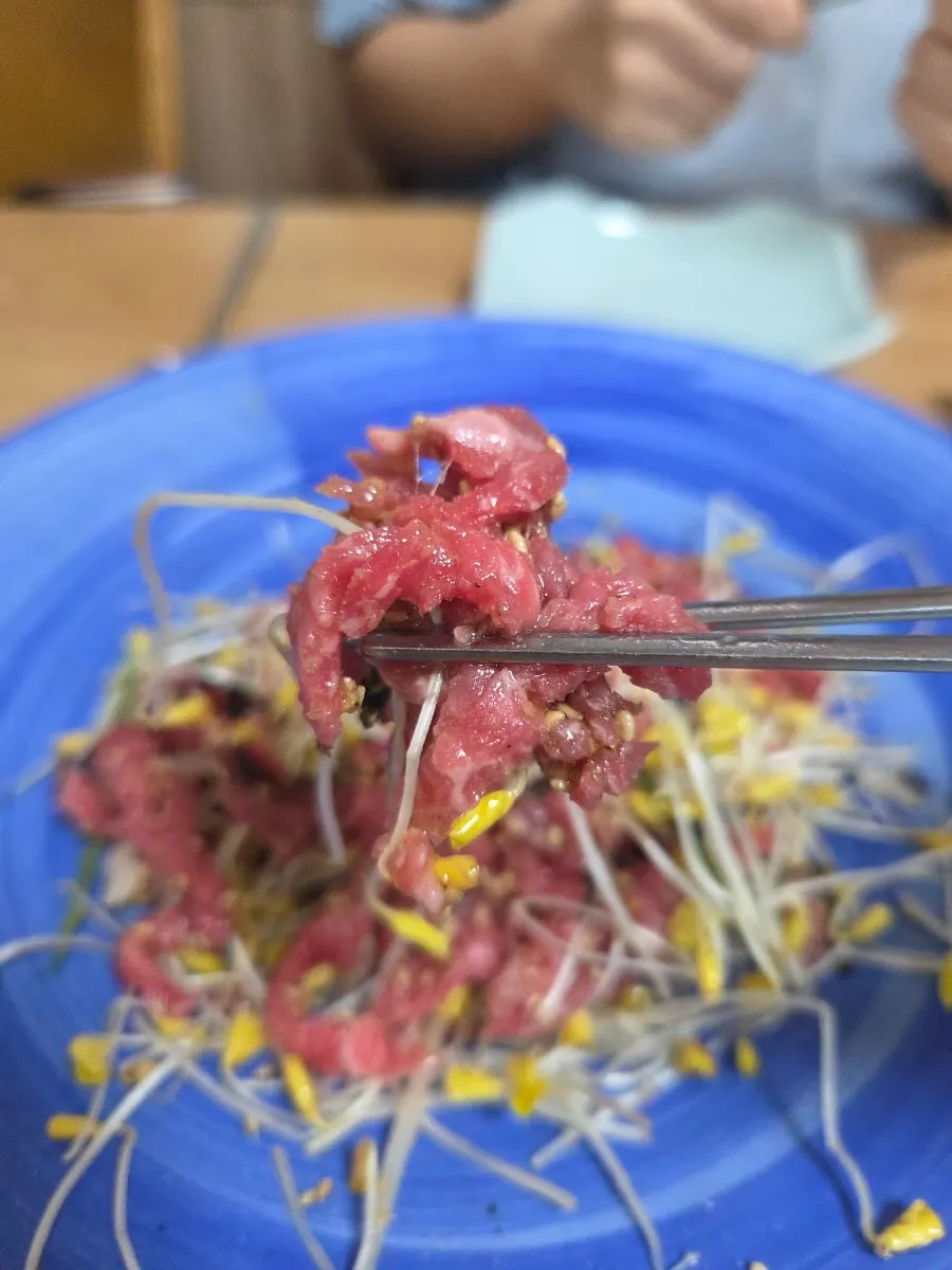 A bite of hanwoo beef tartare picked up with buckwheat sprouts