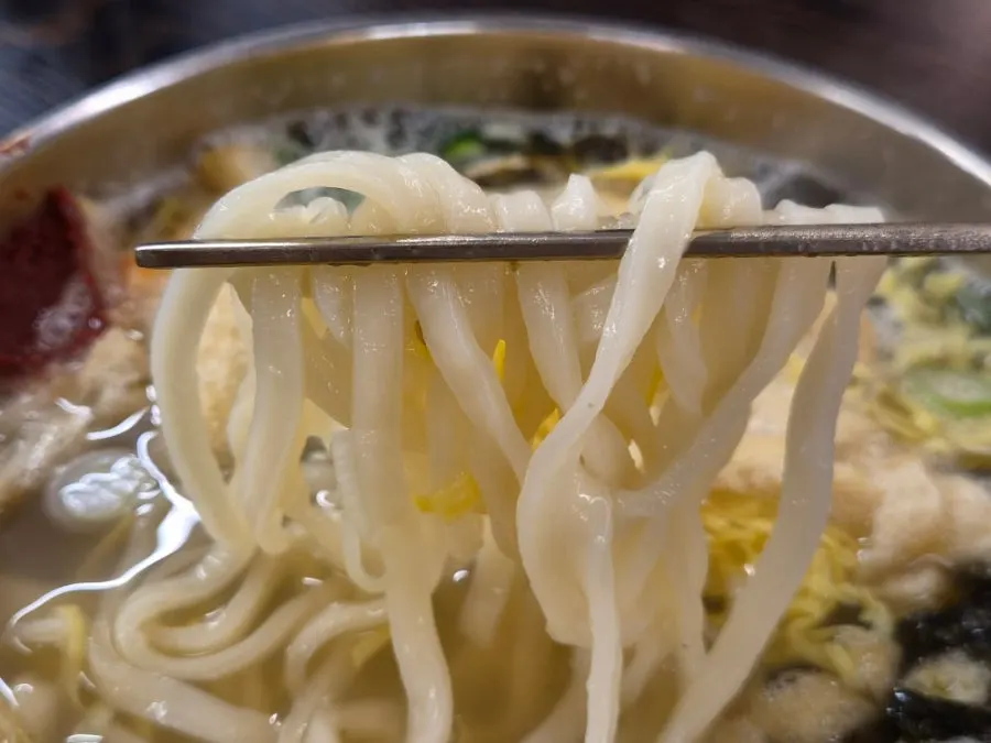Chewy kalguksu noodles lifted up on chopsticks