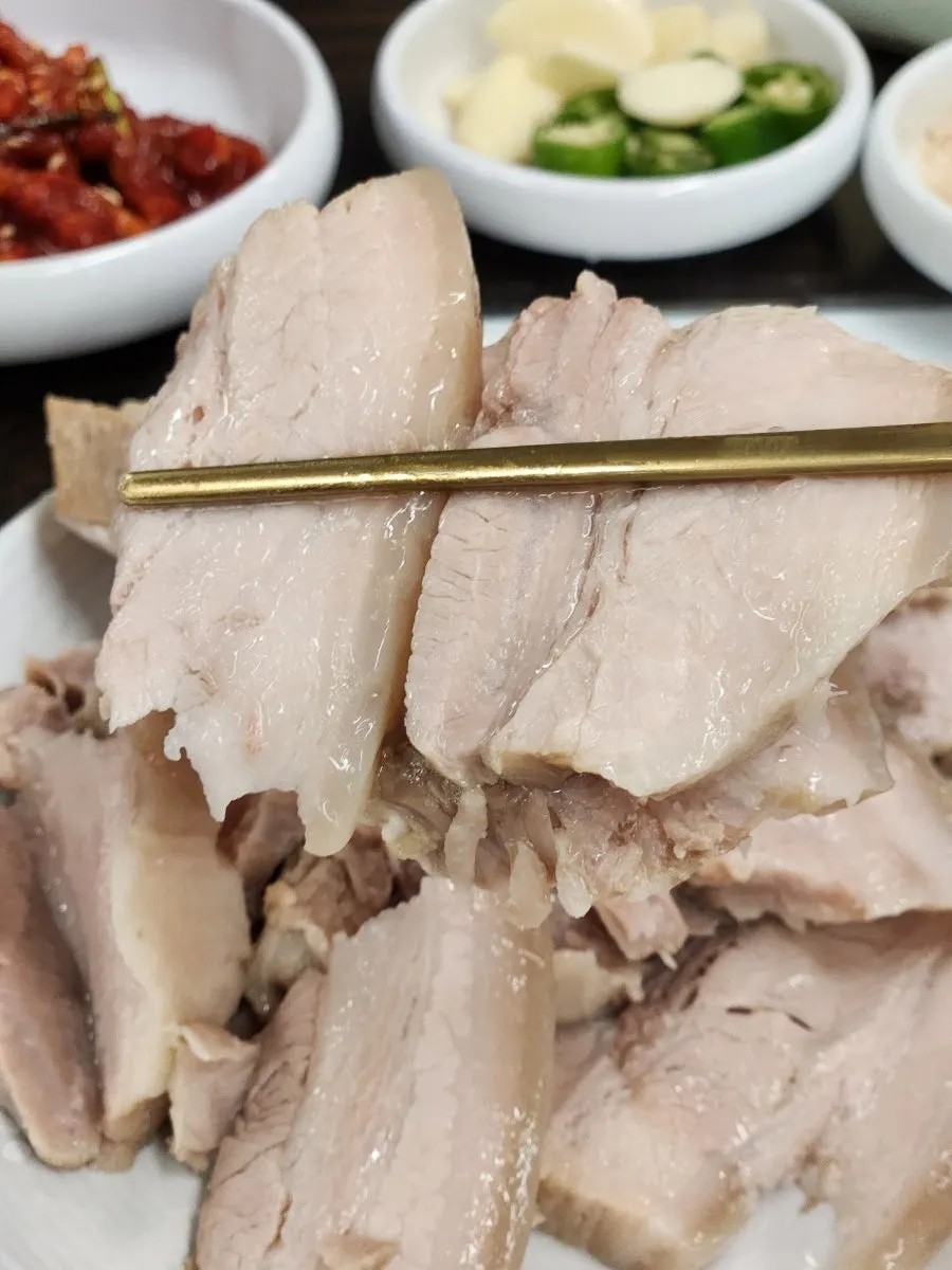 Two pieces of bossam held with chopsticks