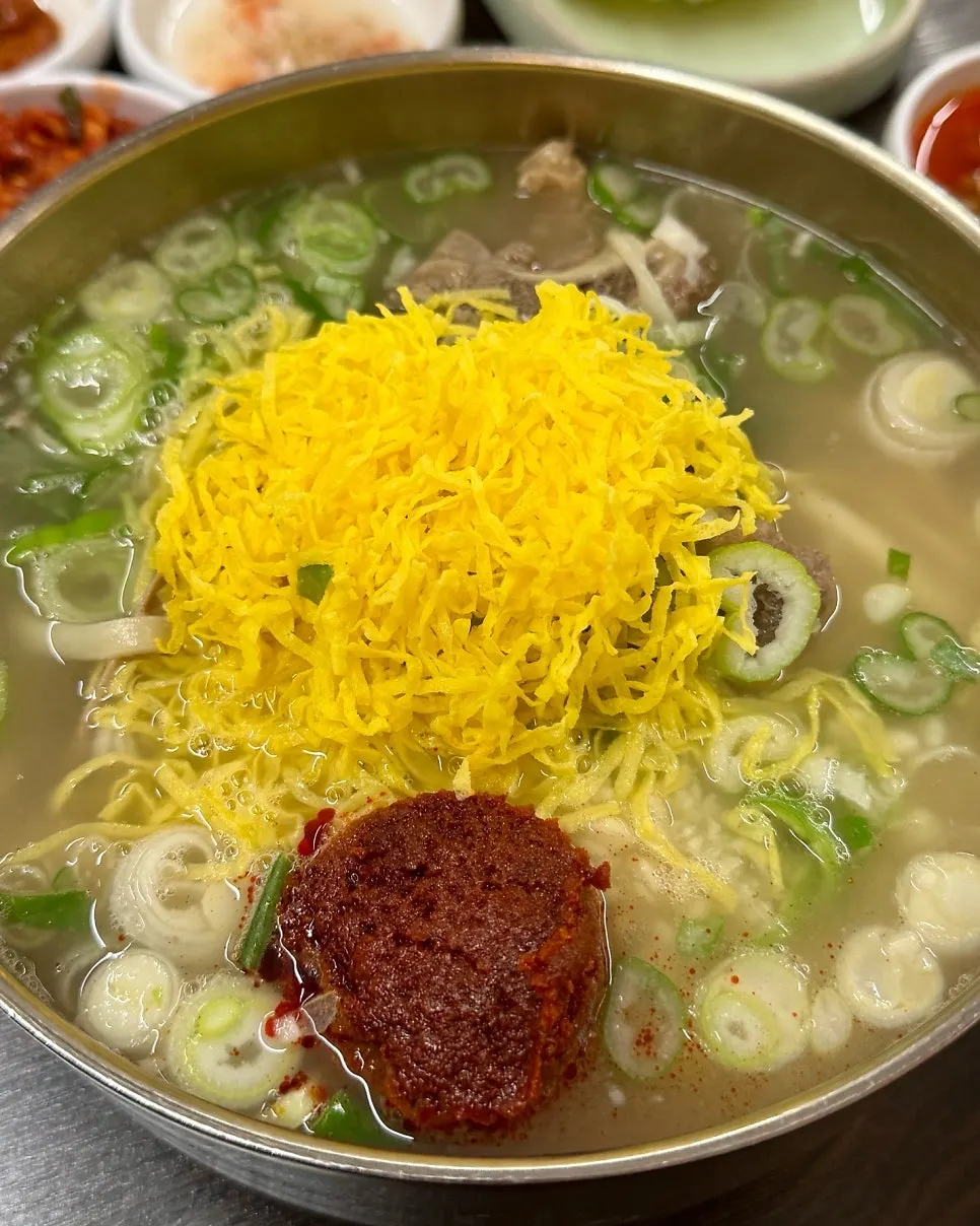Spicy bone kalguksu topped with egg ribbon and scallions