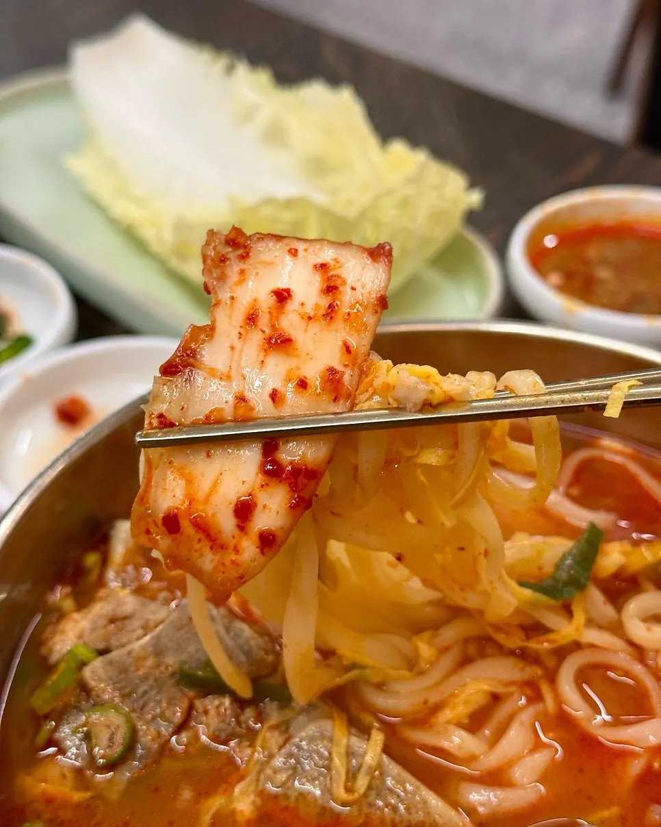 A bite of bone kalguksu noodles with napa cabbage kimchi
