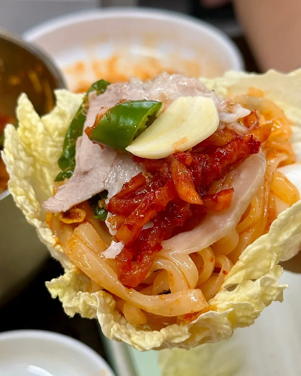 A wrap of baby napa cabbage with bibim kalguksu and bossam on top