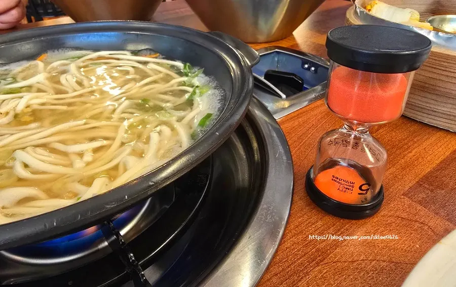 Kalguksu noodles added to clam broth pot with a sand timer