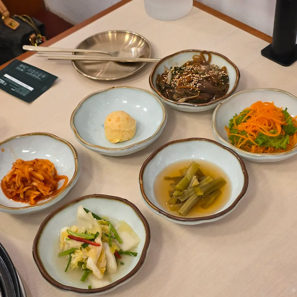 A spread of side dishes at Okryeon Galbi including white kimchi and japchae