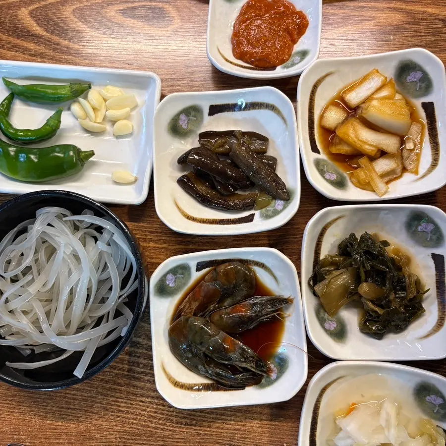 Side dishes including pickled onions, eggplant, and white kimchi