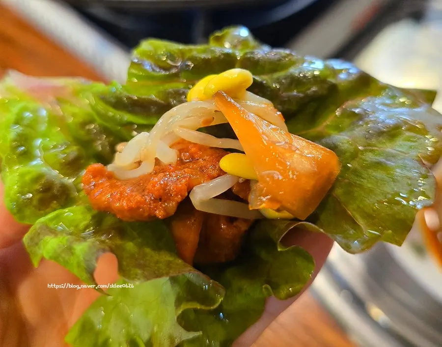 A bite of gochujang jumulleok wrapped in lettuce