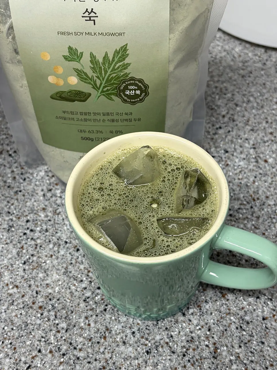 A cup of mugwort soy milk with ice floating in it