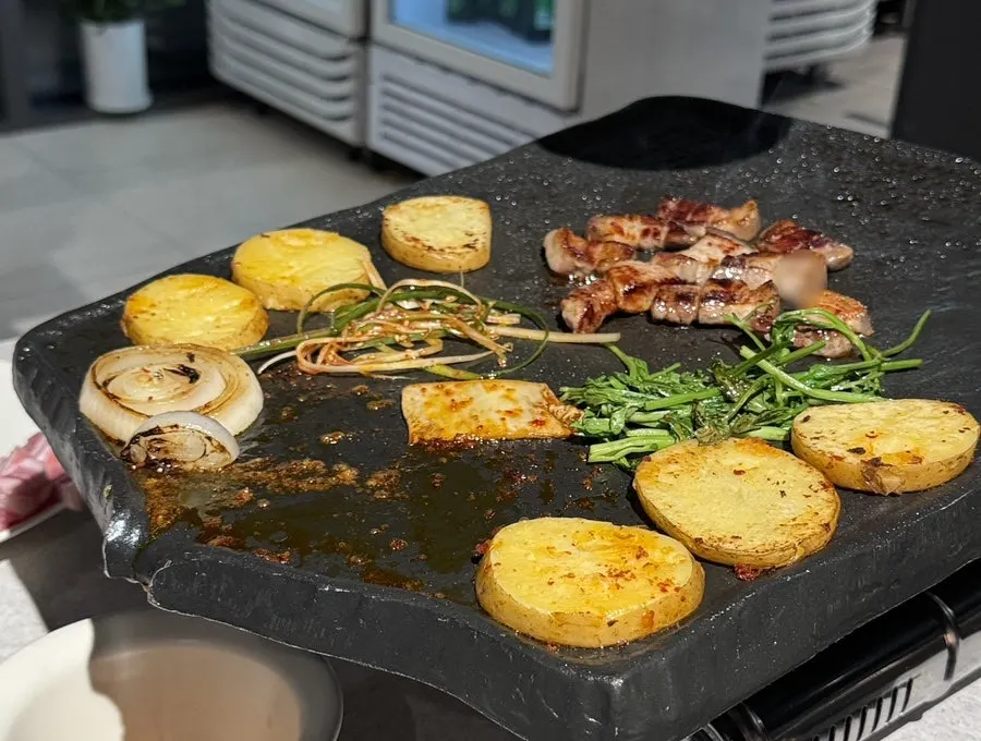 Meat and side vegetables filling the stone plate as they grill
