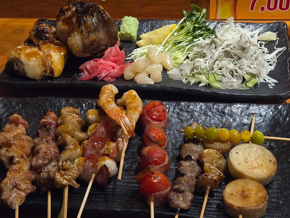 A table with skewers, grilled sea bass, and beer