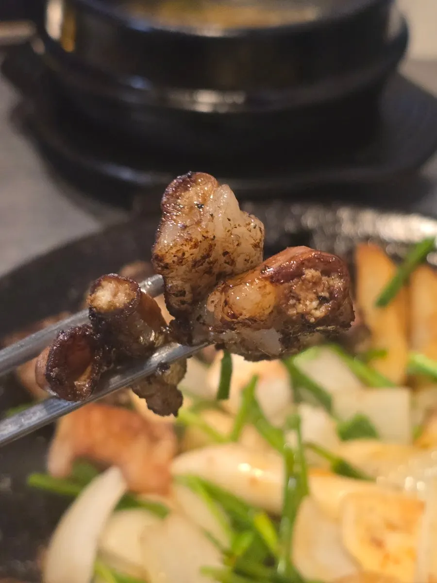 Picking up two pieces of gopchang to dip in the sauce
