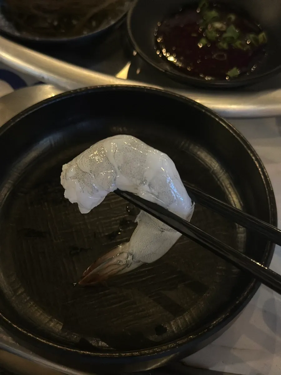 A piece of raw shrimp held with chopsticks