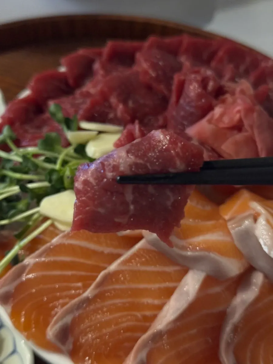 A piece of beef sashimi held with chopsticks