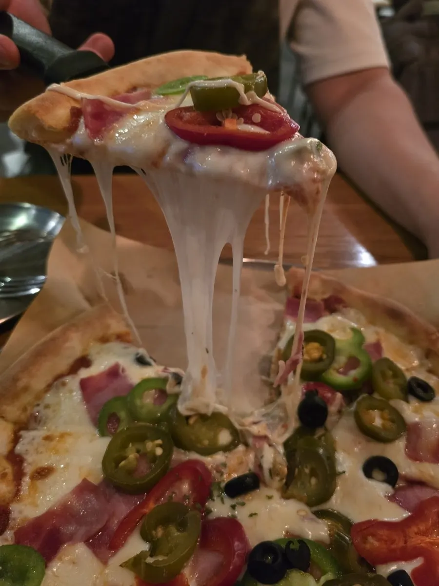 A slice of bacon jalapeño pizza with cheese stretching long
