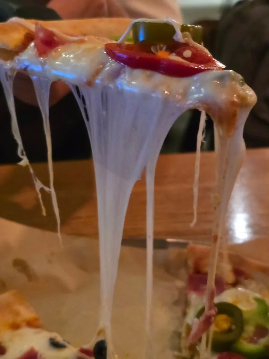 Close-up of stretching cheese on a lifted pizza slice