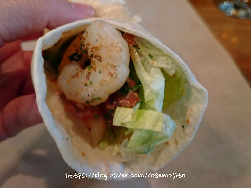 Shrimp taco rolled up and held by hand