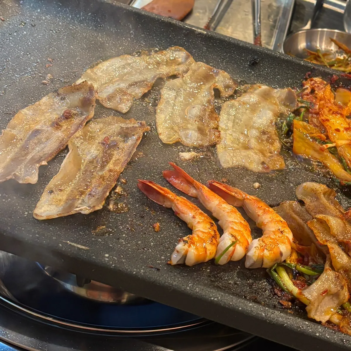 Pork belly, shrimp, and kimchi grilling together on the pan
