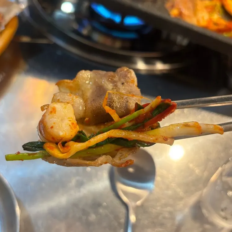 A bite of pork belly topped with shrimp and scallion kimchi