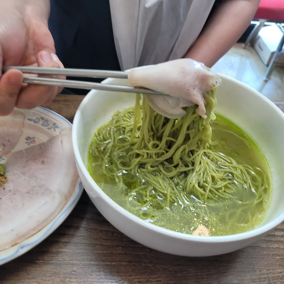 Matcha noodles lifted with chopsticks