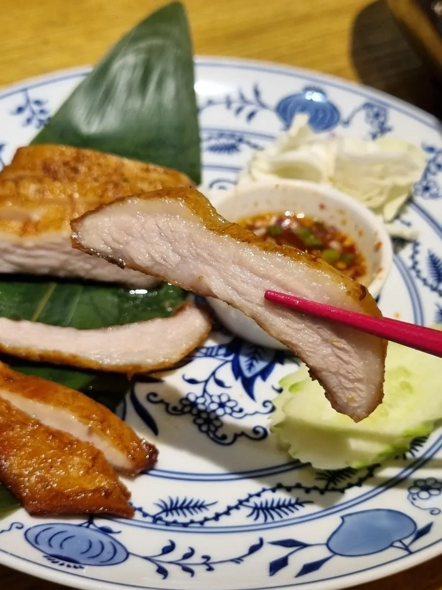 A piece of khor moo yang pork jowl dipped in sauce