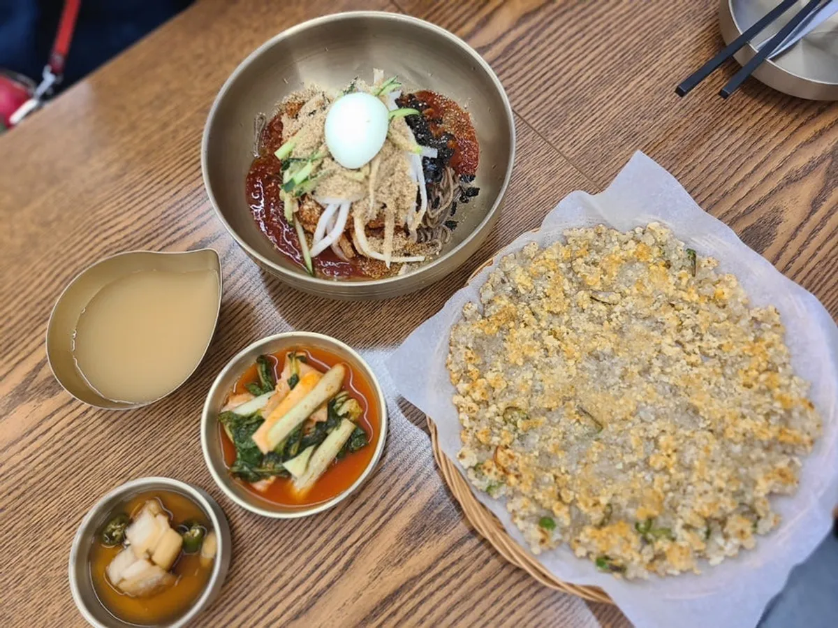 Bibim makguksu topped with vegetables, seaweed flakes, and egg