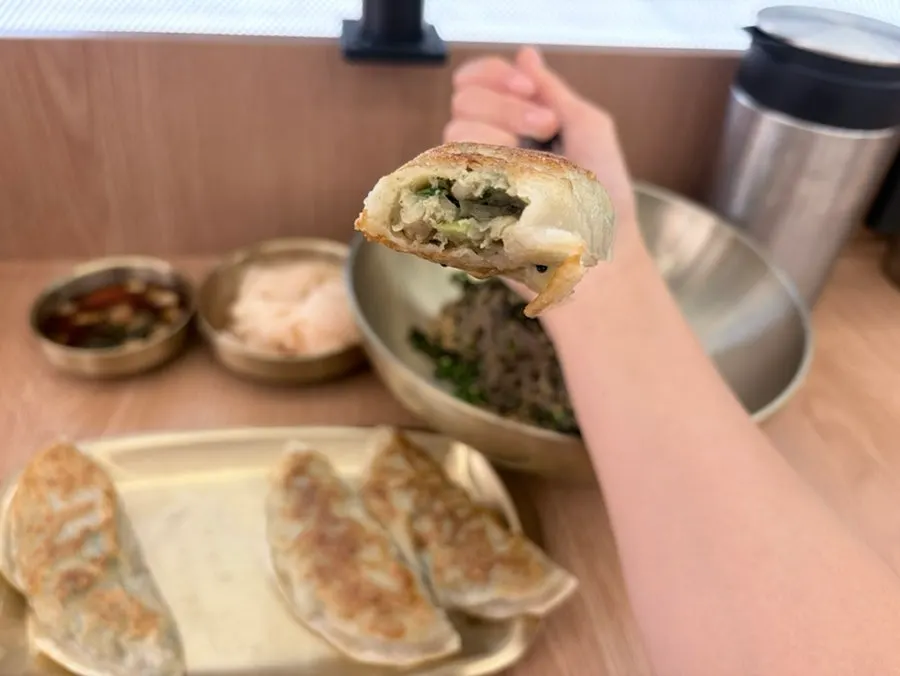 Mandu dipped in sauce, bitten open to show the filling