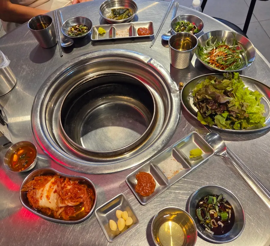 Table of banchan including lettuce, scallion salad, salted shrimp, and wild garlic leaves