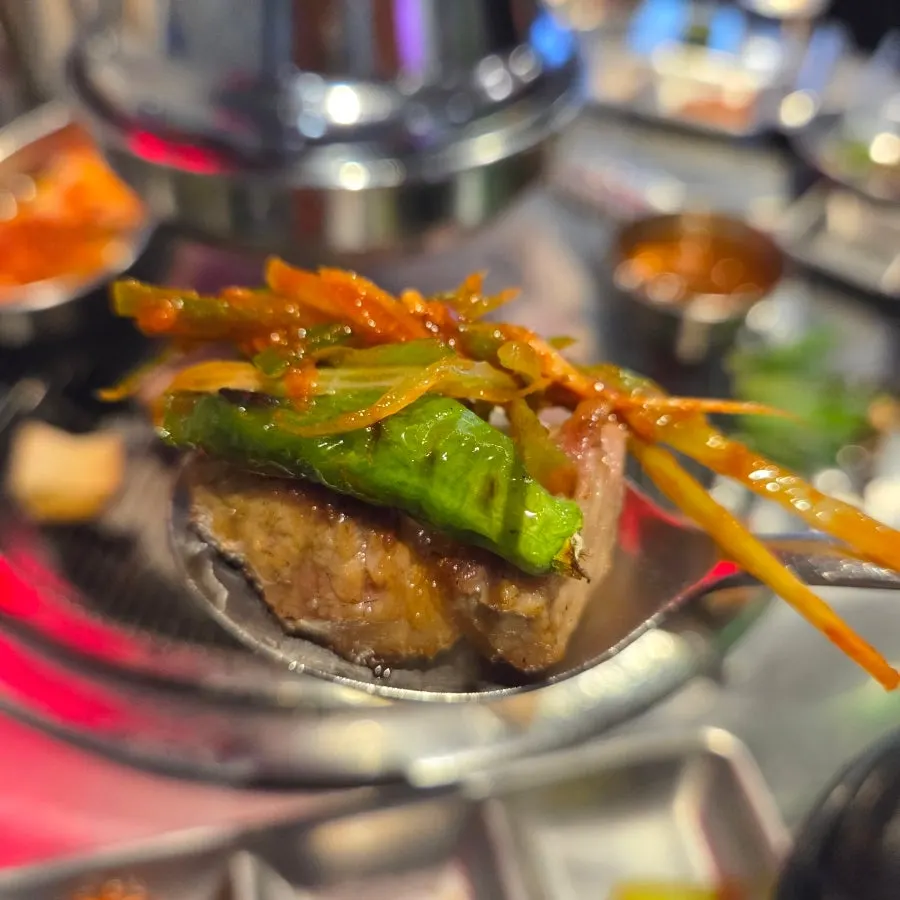 Meat dipped in sauce with a shishito pepper