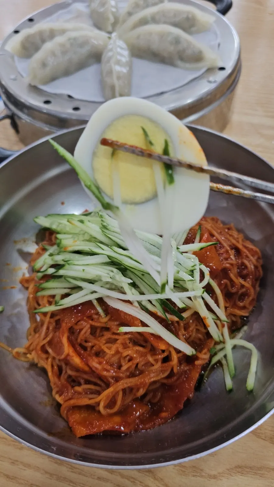 Bibim milmyeon topped with cucumber strips and pickled radish