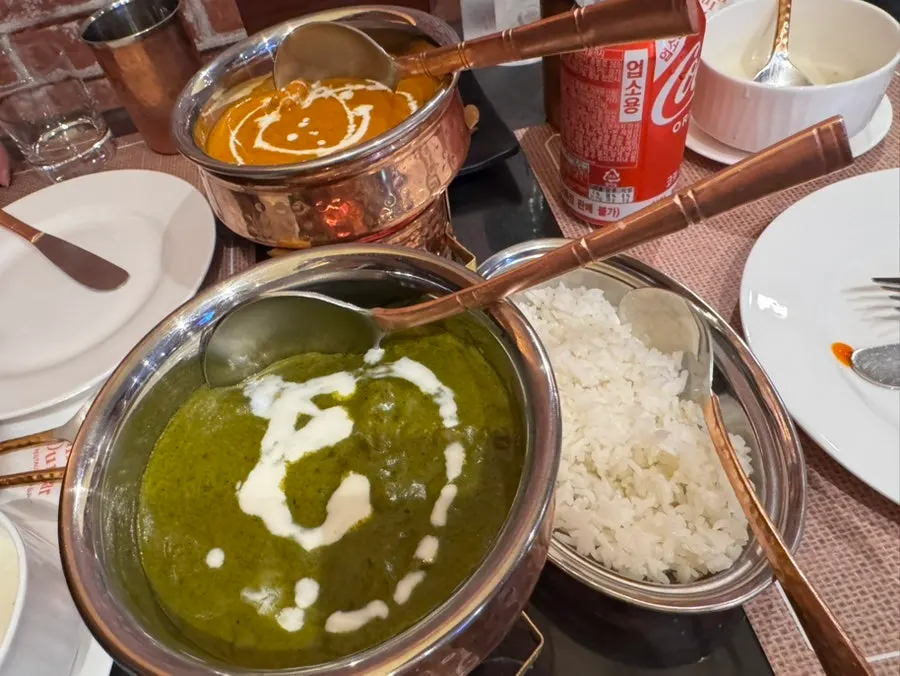 Dua mangkuk kari, butter chicken oranye dan palak paneer hijau