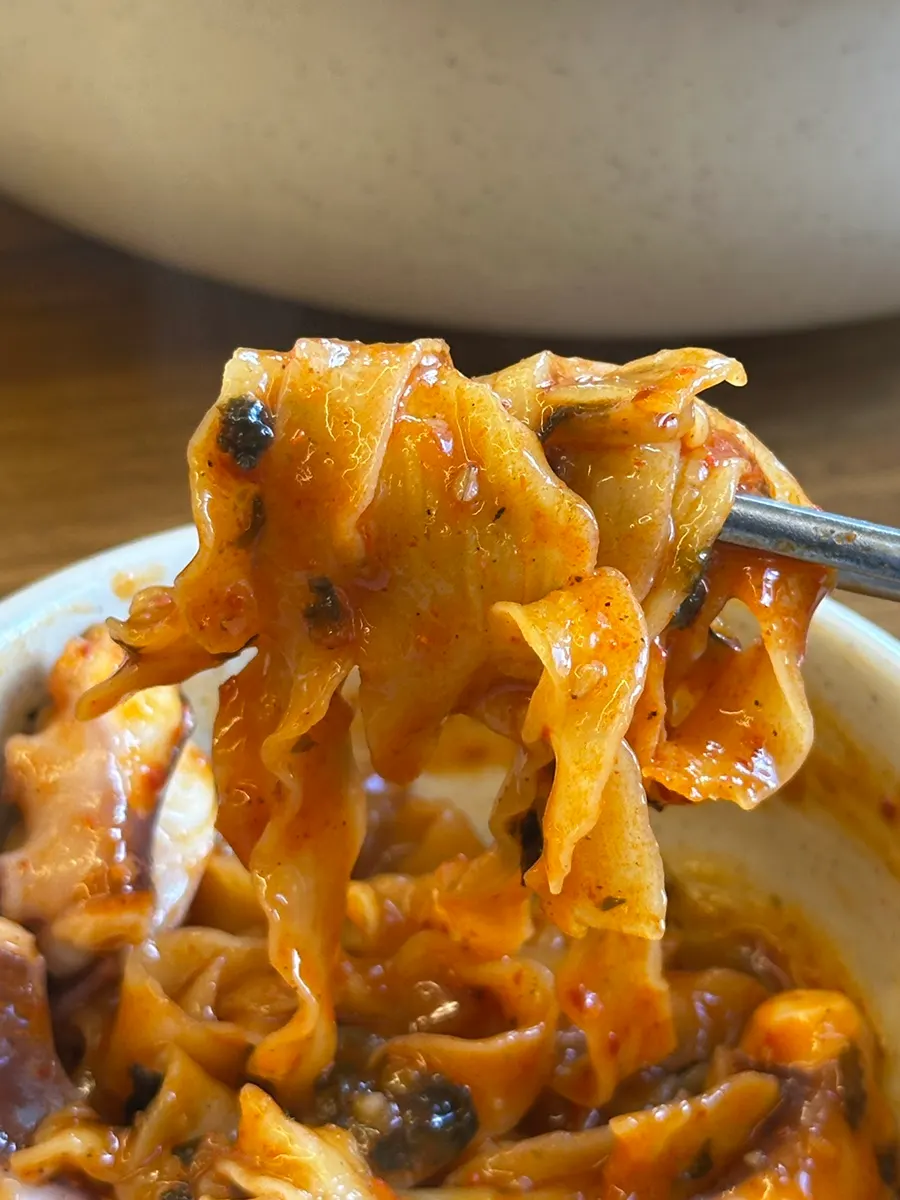 A chopstick-full of kalnakji noodles with a piece of octopus on top