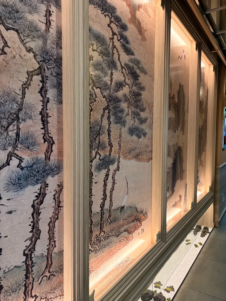 Entrance corridor lined with ink-wash panels of pine trees and cranes