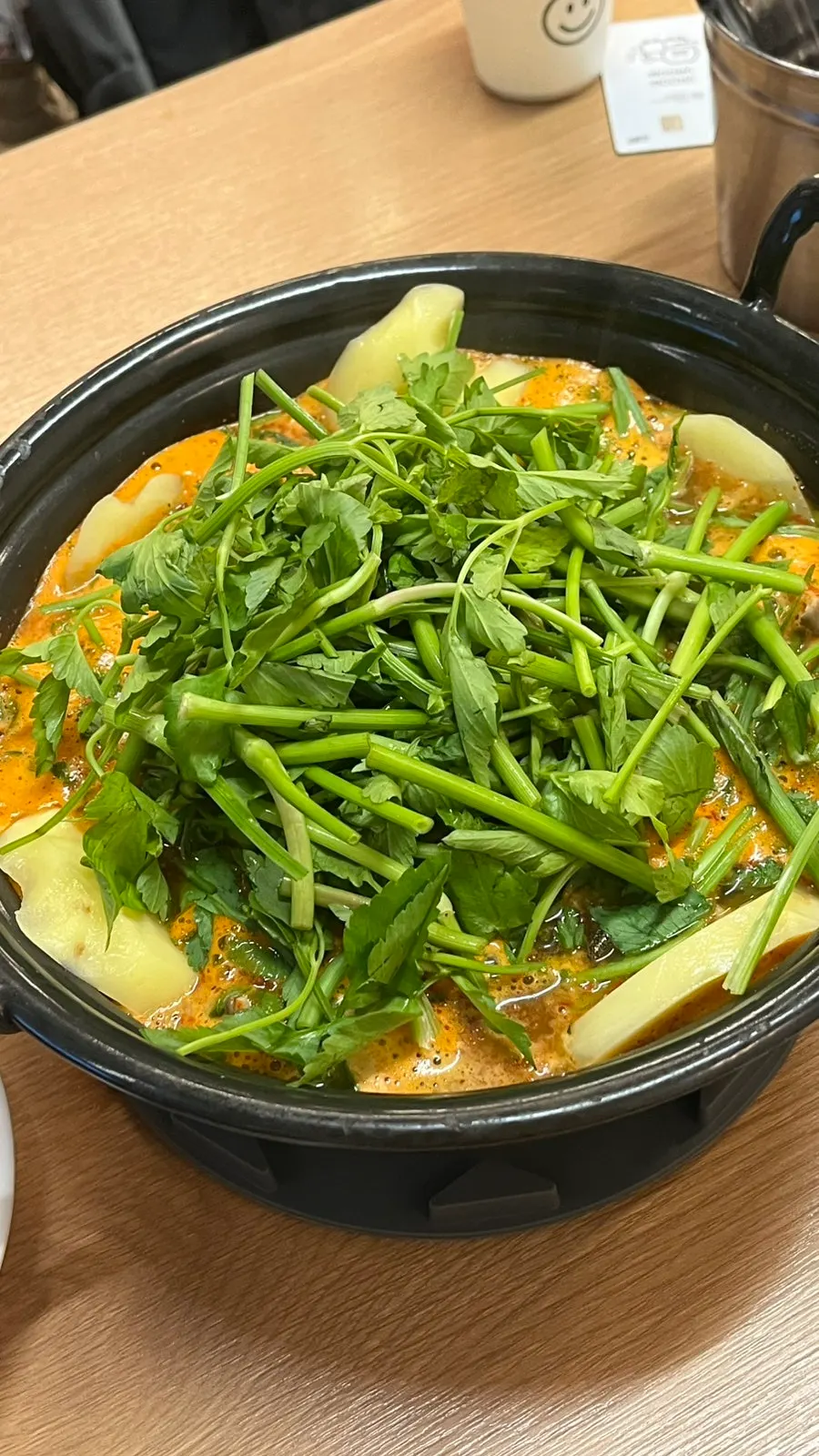 A shabu pot filled with minari and potatoes