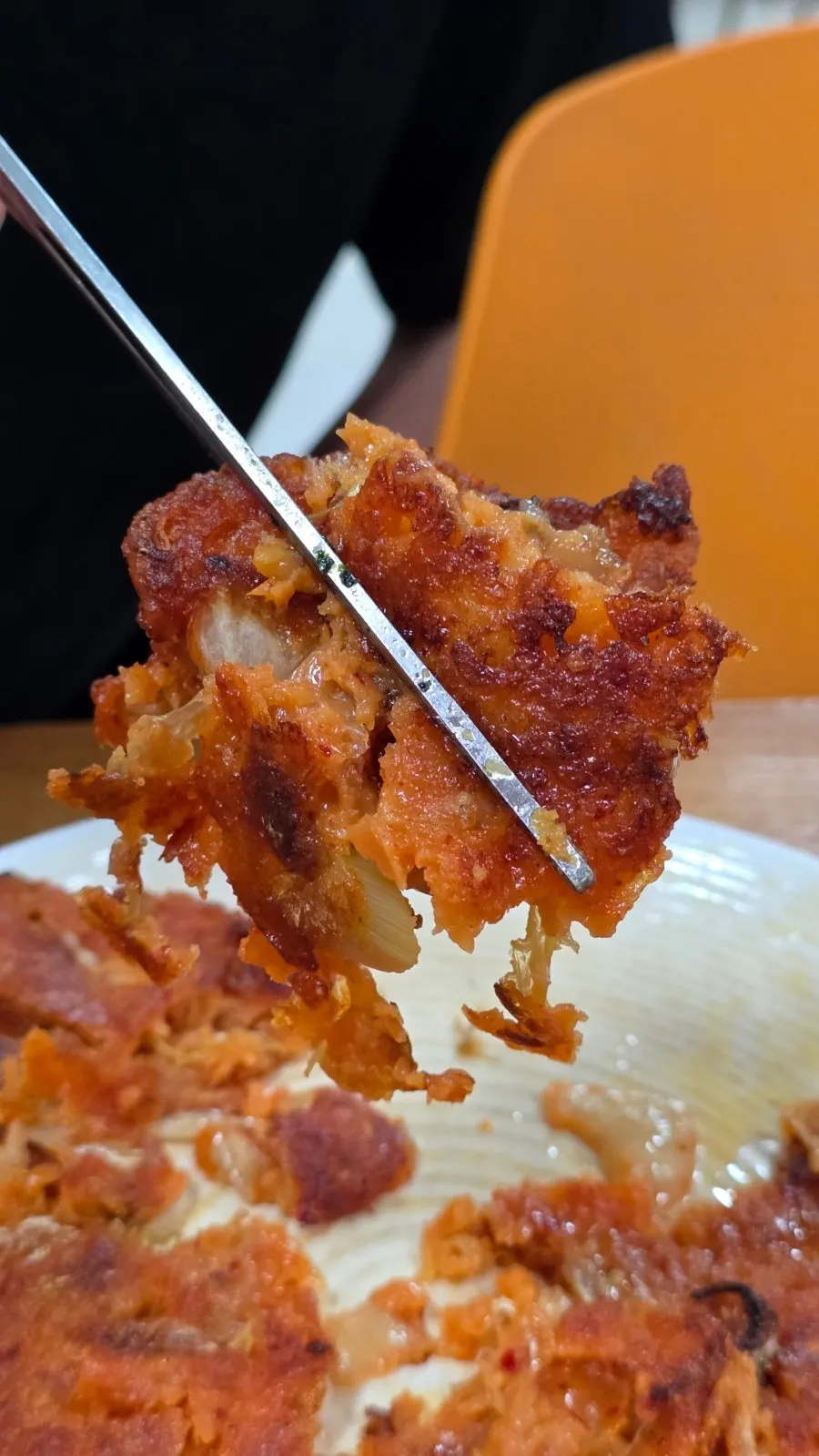 A crispy piece of kimchi pancake lifted with chopsticks