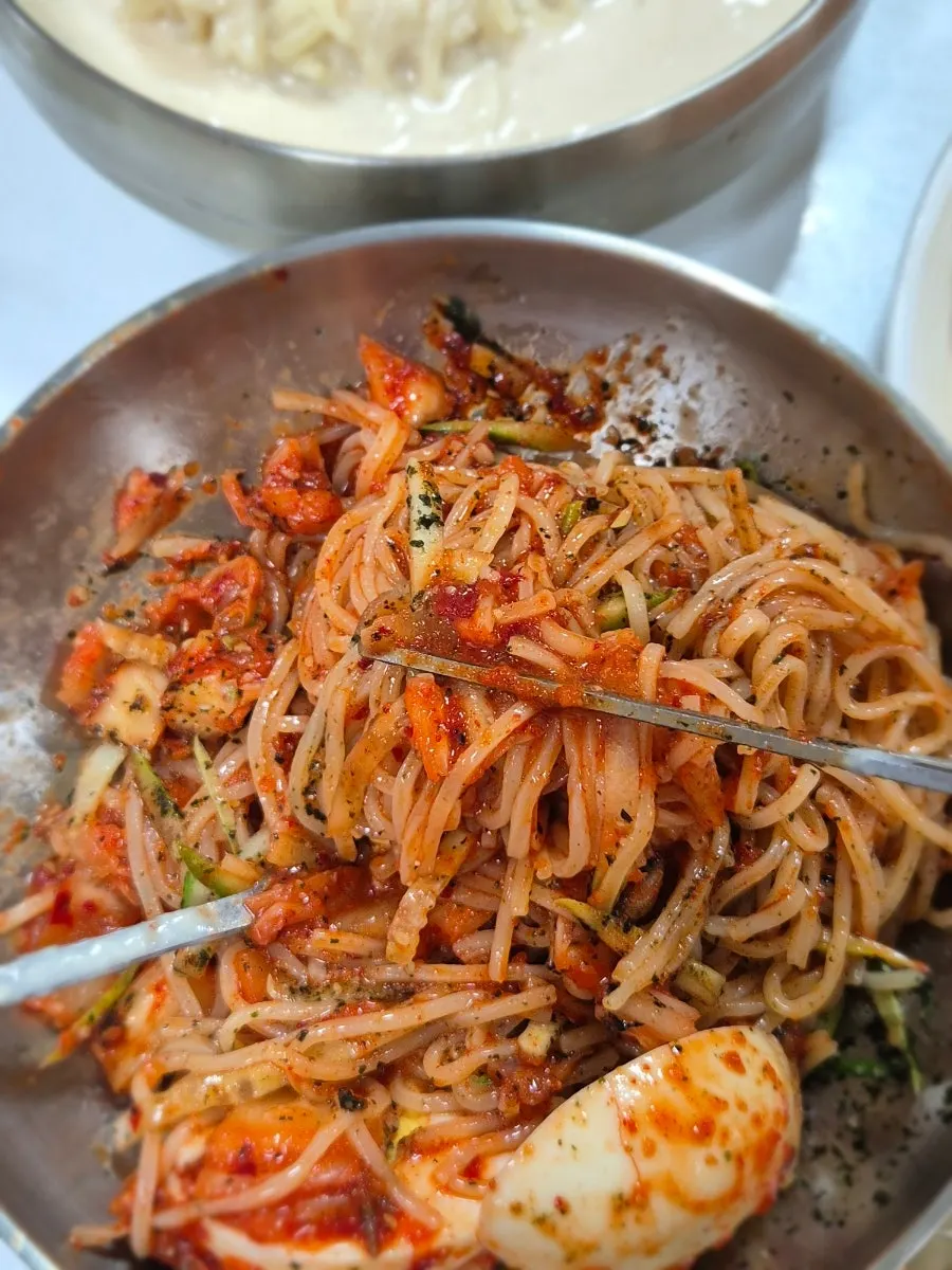 Warm broth served alongside the bibim guksu