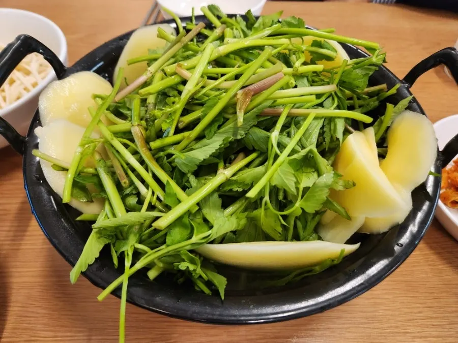 Pot of clear broth piled high with minari
