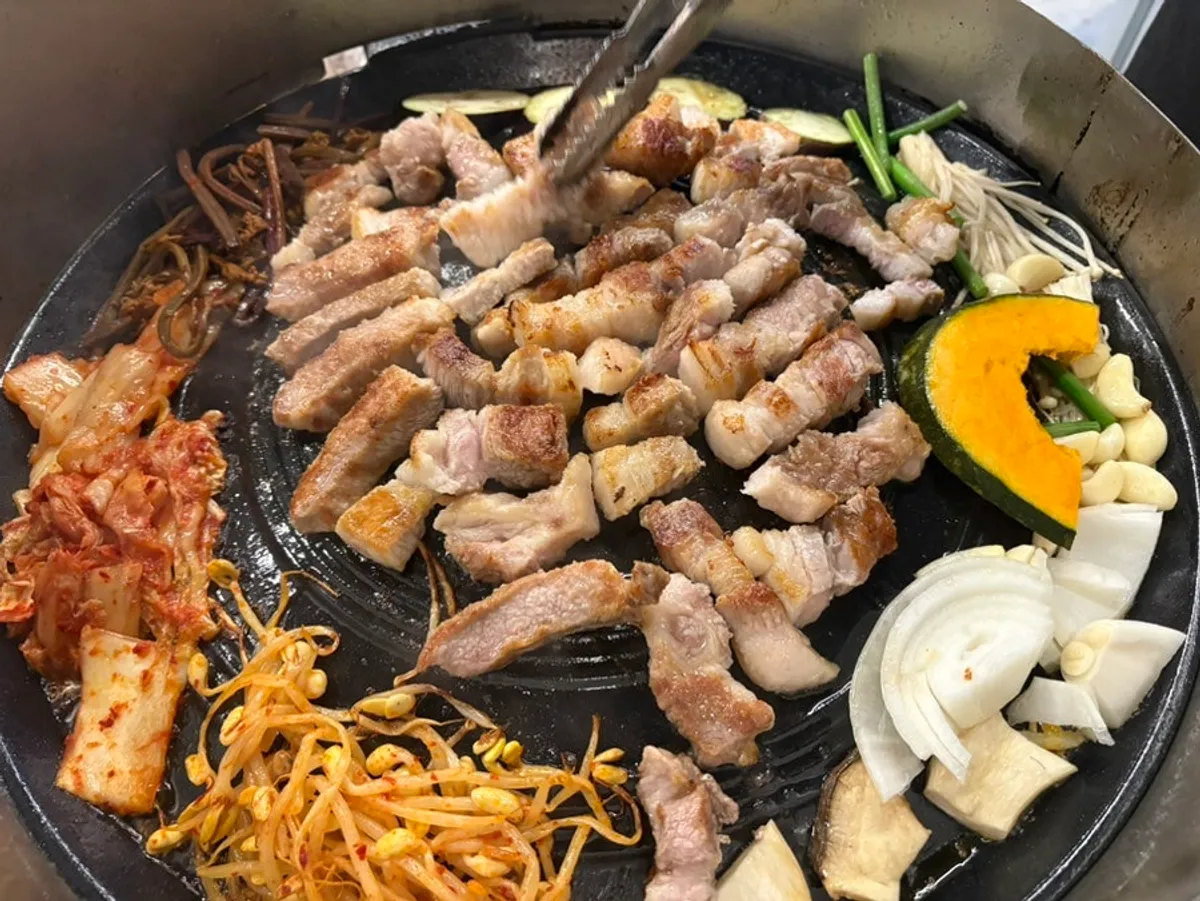 Samgyeopsal and pork neck grilling on the cast-iron lid