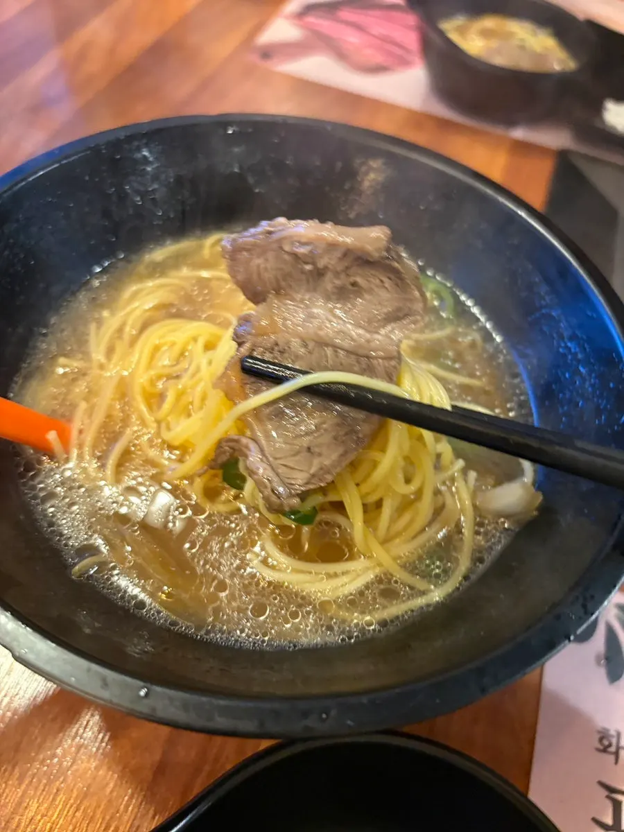 Noodles and broth in a black bowl topped with beef