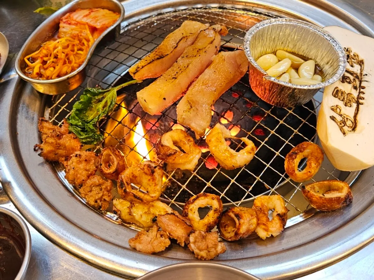 Table with charcoal-grilled meat and a drink glass