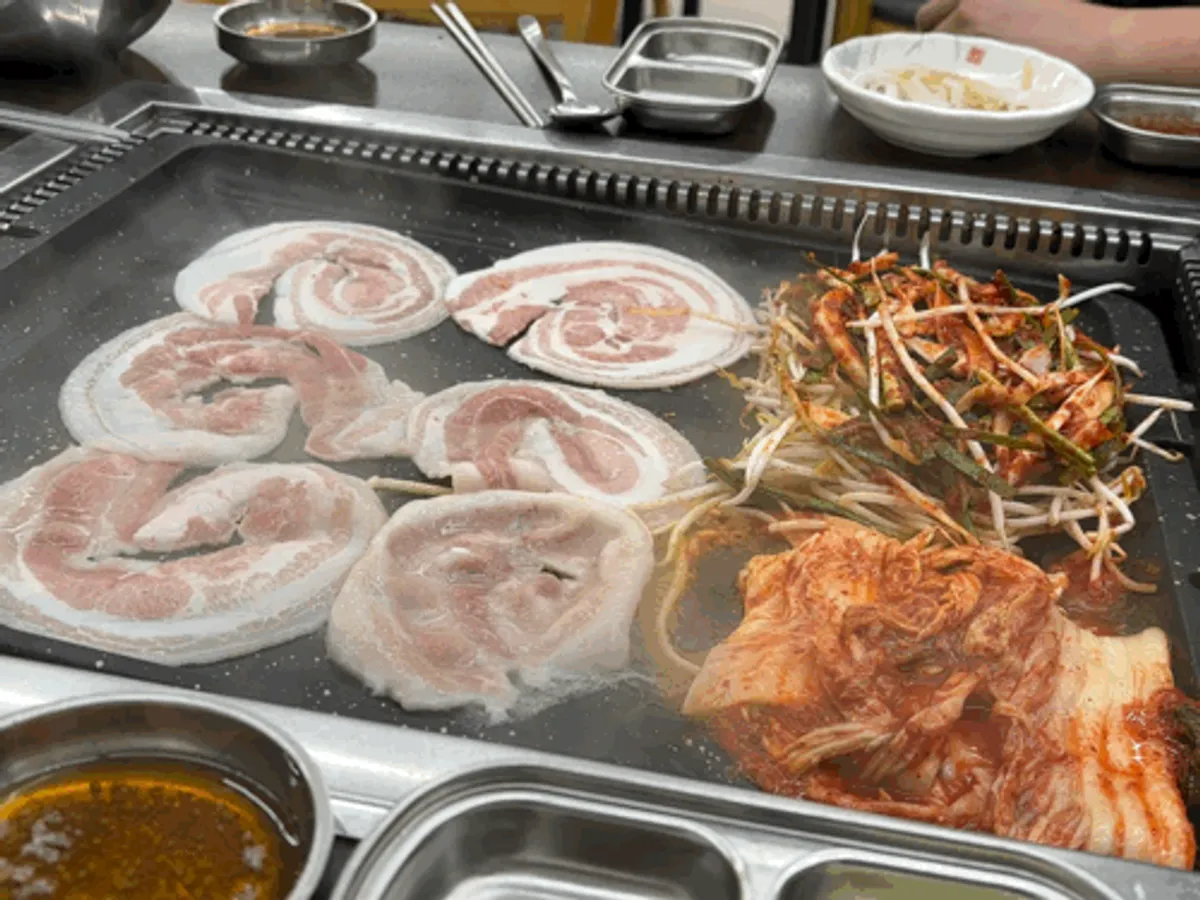 Bean sprouts and meat being fried at the edge of the grill