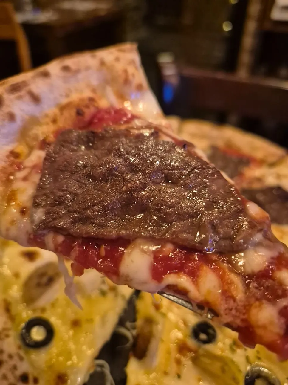 Slice of Manjo pizza loaded with meat toppings